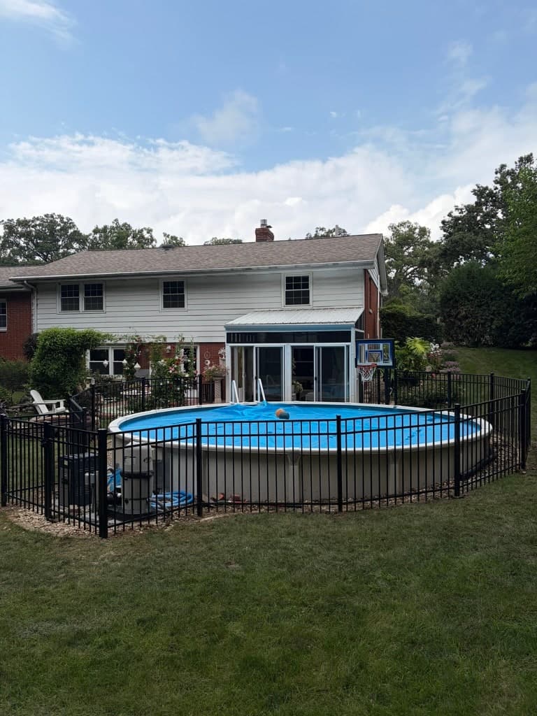 Black aluminum picket fence enclosing an above-ground pool behind a two-story house