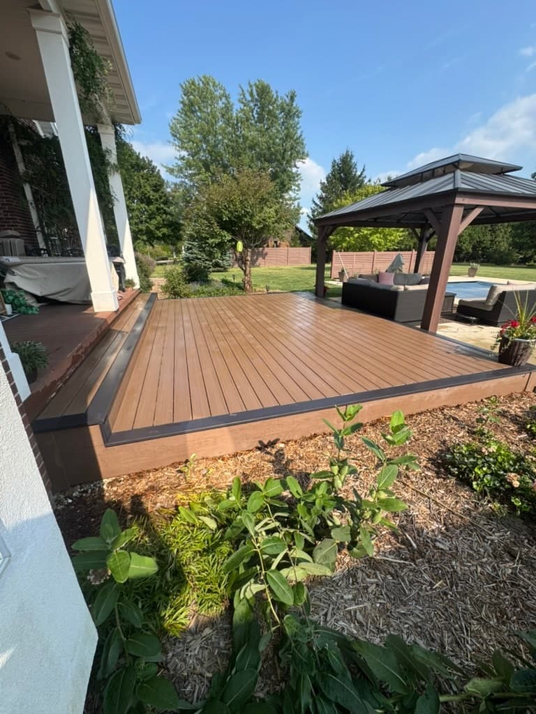 Ground-level composite deck with a darker picture-frame border, stepping down from a covered porch toward a gazebo and pool