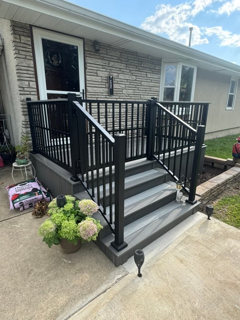 Grey composite front porch and steps with black aluminum railing on a stone-faced ranch house