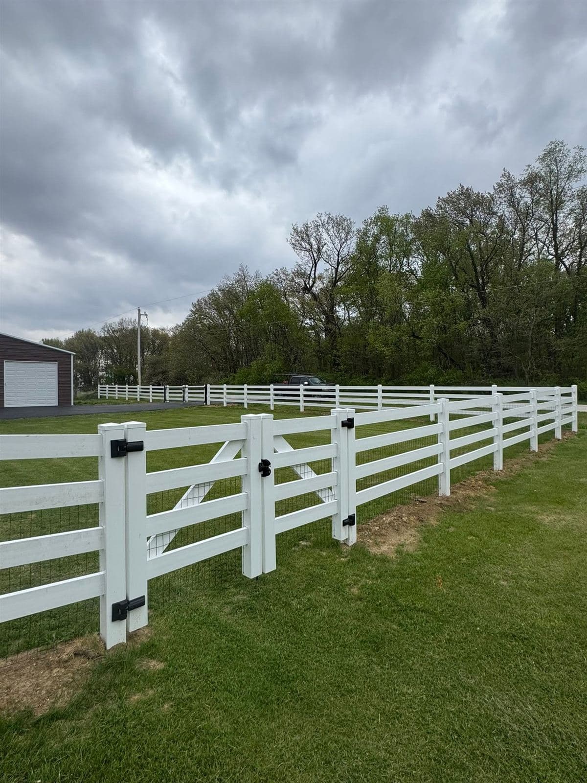 White vinyl ranch rail fence with a braced single gate and wire mesh backing, on a country property