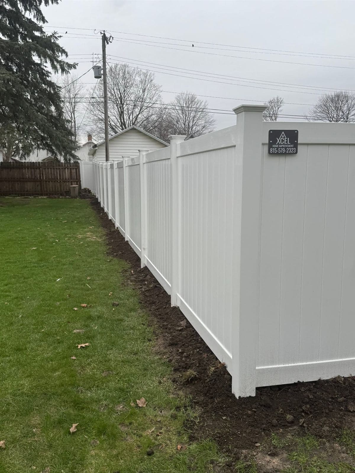 White vinyl privacy fence line with Xcel job sign