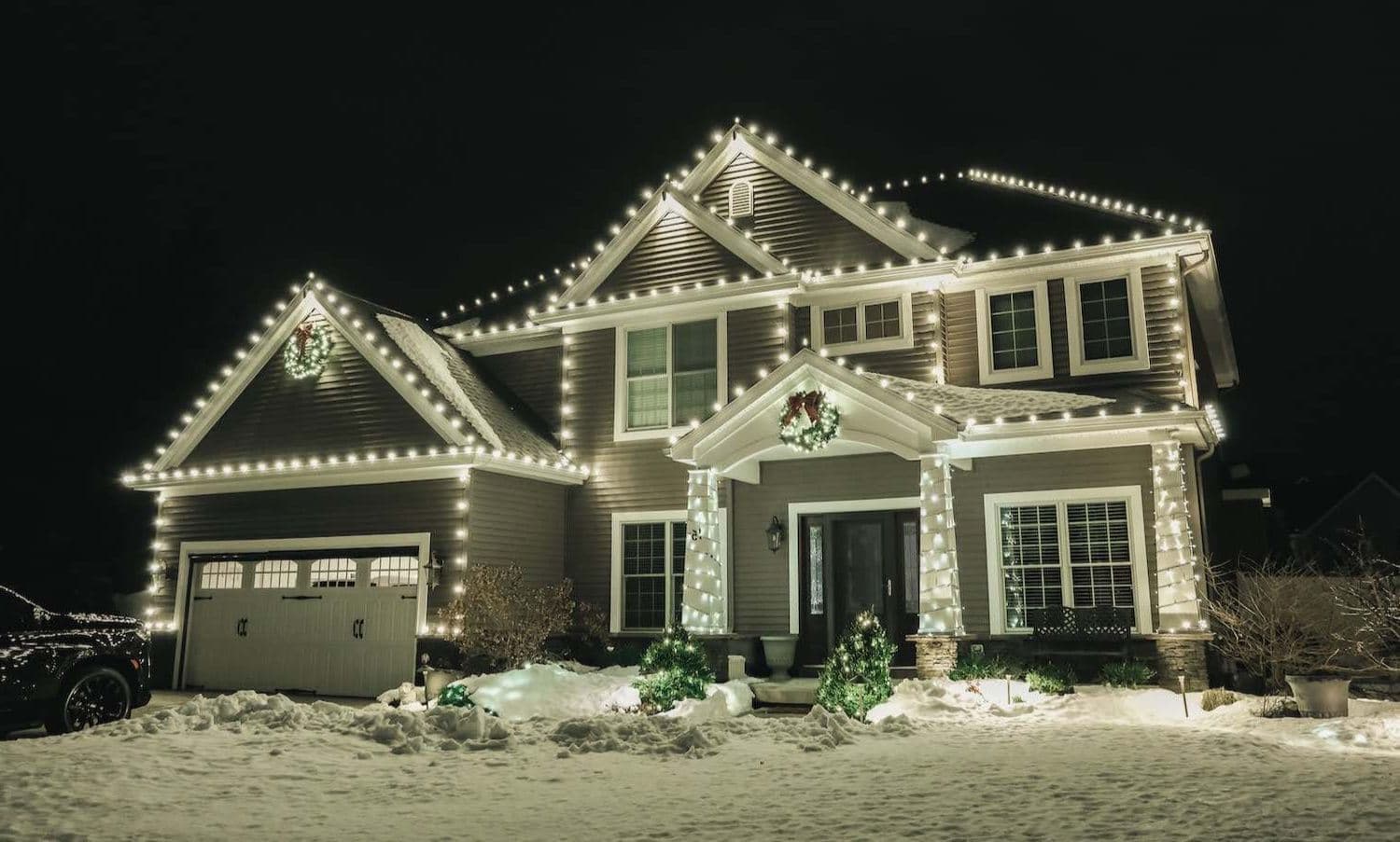 Two-story home outlined in warm white holiday lighting at night