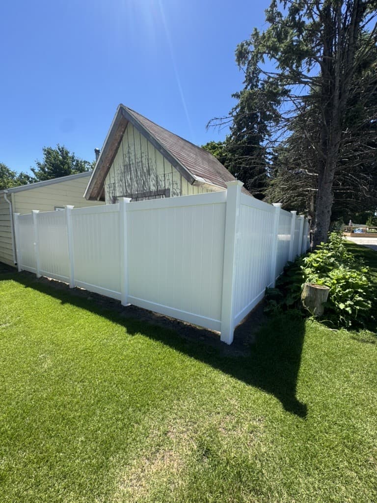 White vinyl privacy fence run along a mown back yard