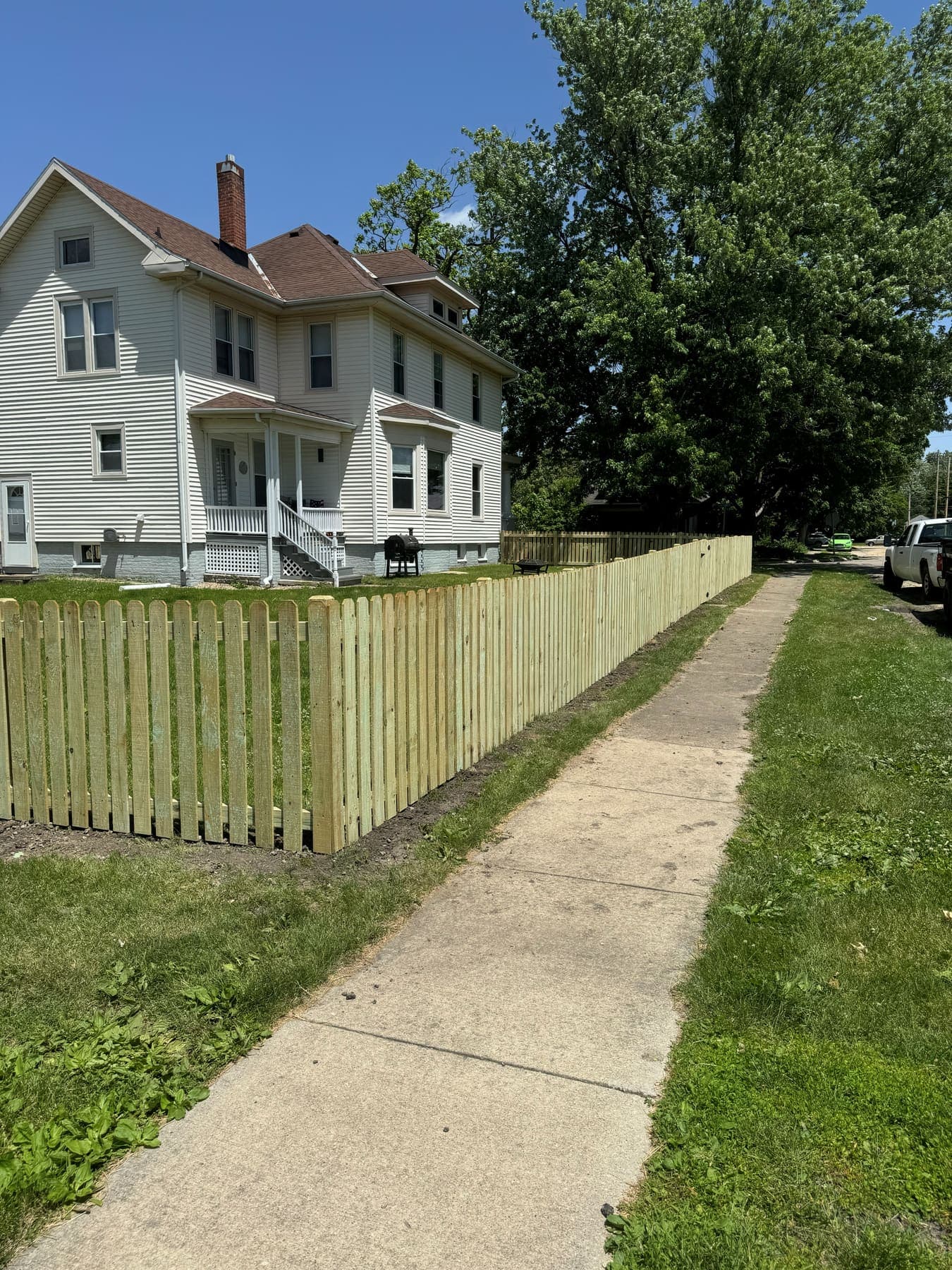 Treated wood picket fence running the length of a front lot beside a public sidewalk