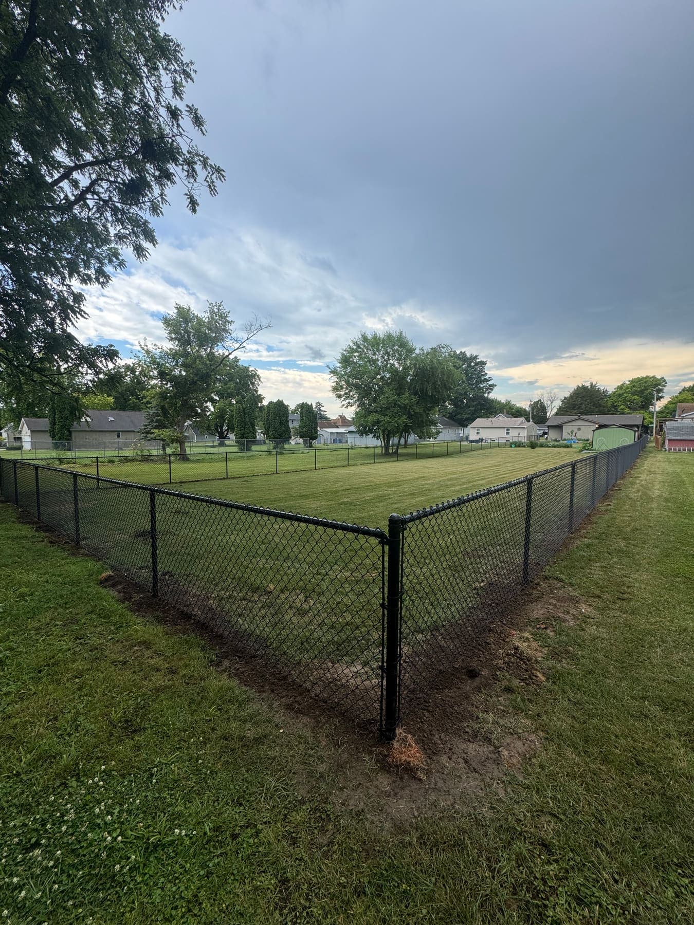 Black vinyl-coated chain-link fence turning a corner post around a large open yard, installed by Xcel Outdoor Living