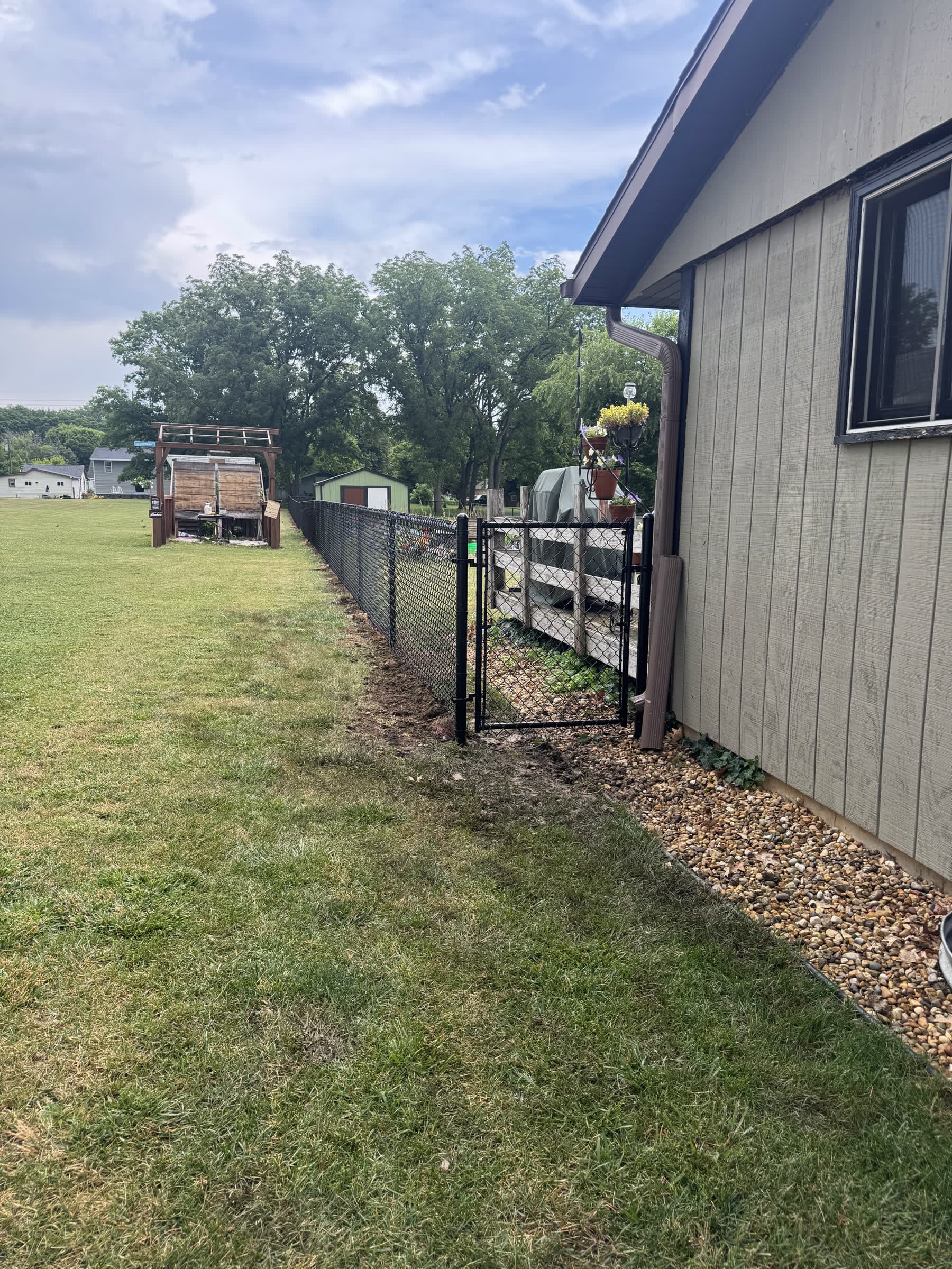 Black vinyl-coated chain-link fence and walk gate running along the side of a house, installed by Xcel Outdoor Living