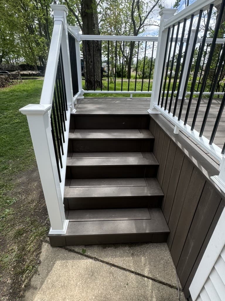 Composite deck stairs with white posts and black aluminum balusters, built by Xcel Outdoor Living