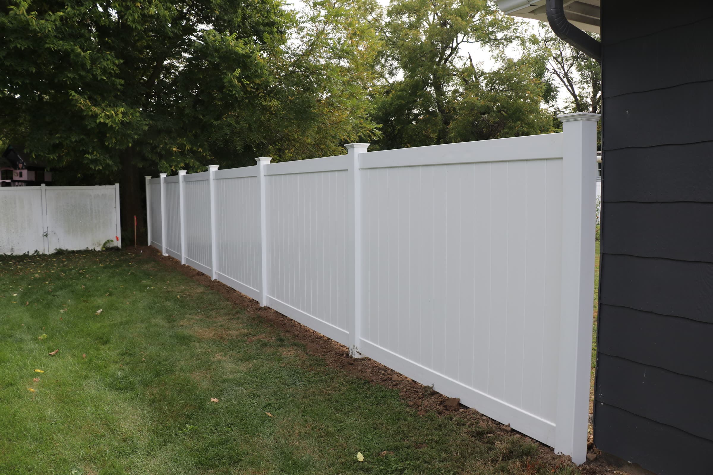 White vinyl privacy fence against a house with charcoal siding, installed by Xcel Outdoor Living
