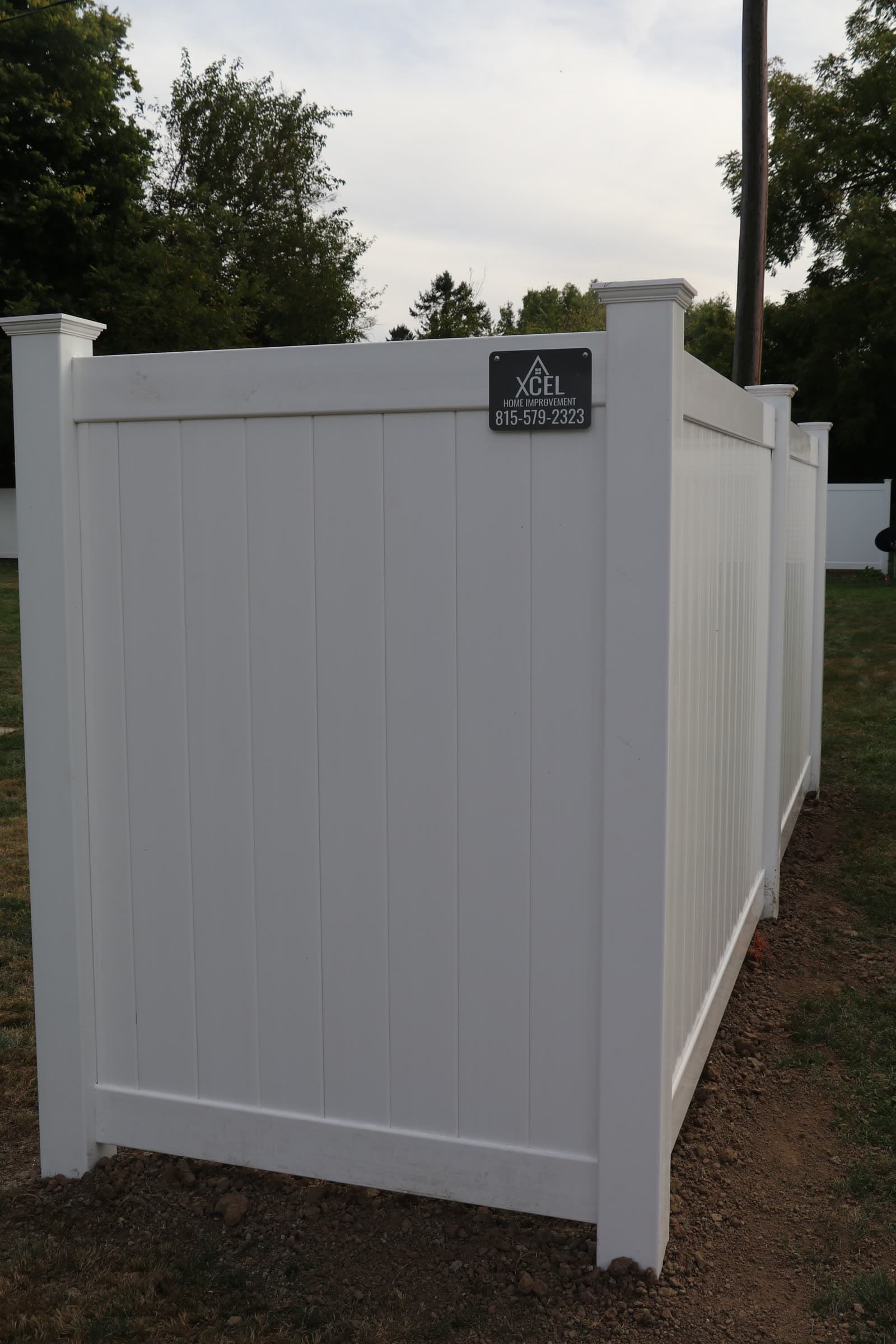 Finished white vinyl privacy fence carrying the Xcel job sign and phone number